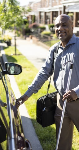 Picture of a blind person approaching his car with the help of a walking stick.